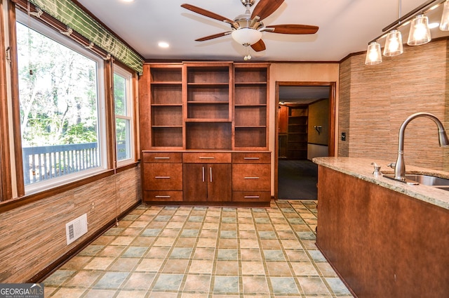 kitchen with light stone counters, visible vents, ceiling fan, a sink, and decorative light fixtures