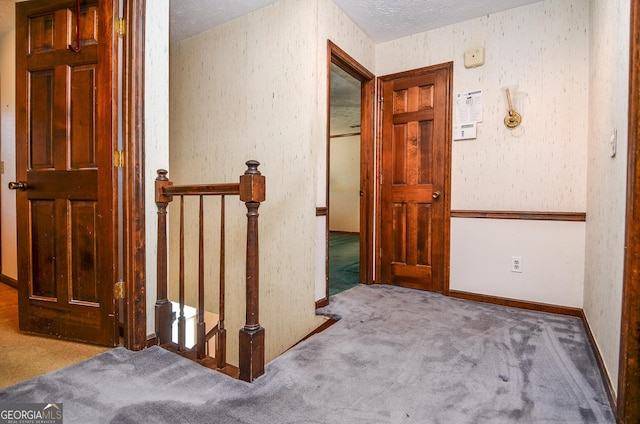 hall featuring an upstairs landing, carpet flooring, a textured ceiling, and baseboards