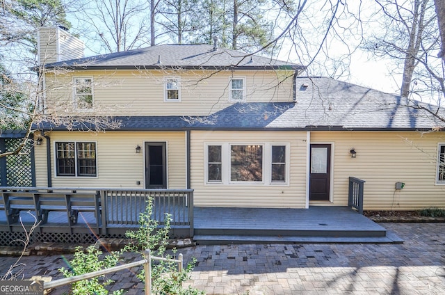 rear view of house with a deck, a shingled roof, and a chimney