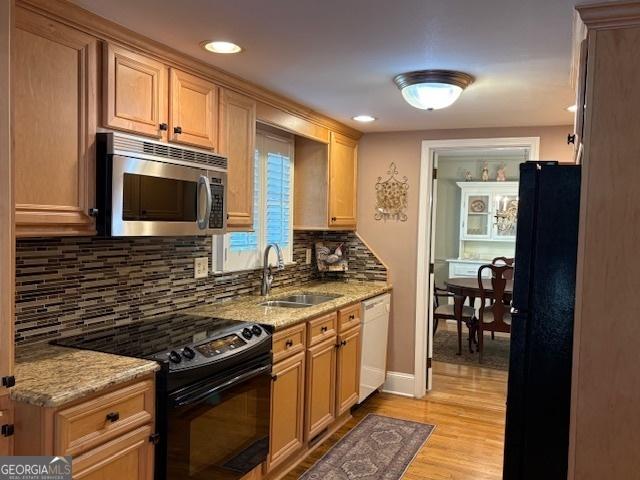 kitchen featuring black appliances, light stone countertops, light wood finished floors, and a sink