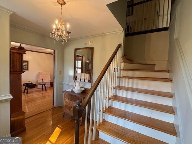 stairway with a notable chandelier, wood finished floors, and ornamental molding