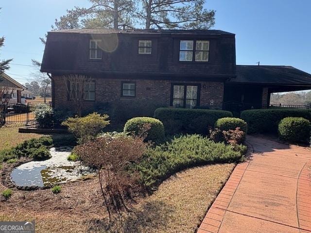 view of front facade with brick siding, roof with shingles, and fence