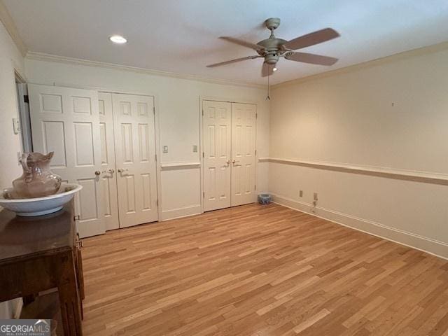 bedroom featuring light wood-style flooring, baseboards, multiple closets, and ornamental molding