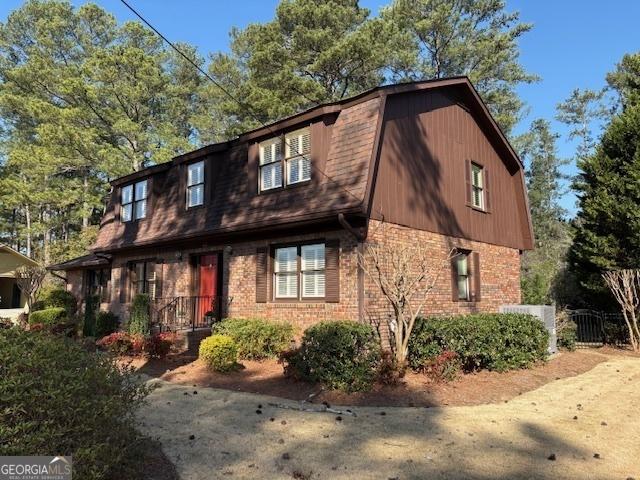 colonial inspired home with brick siding, a gambrel roof, a shingled roof, and fence