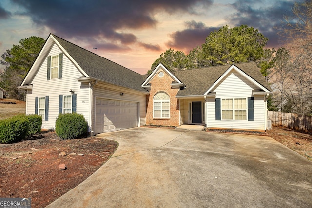 view of front facade with brick siding, a shingled roof, fence, driveway, and an attached garage