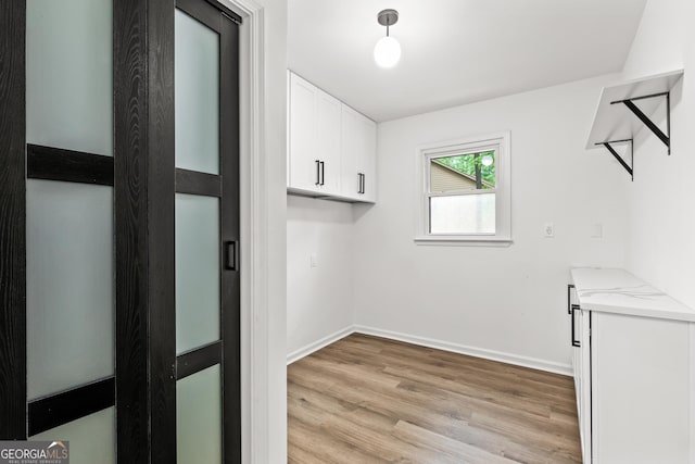 clothes washing area featuring light wood-type flooring and baseboards