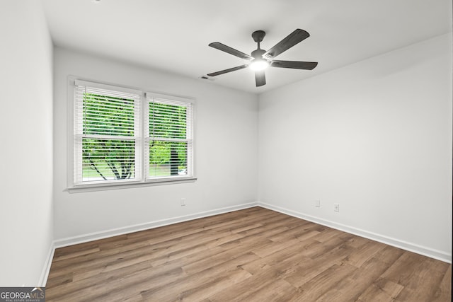 spare room with wood finished floors, visible vents, a ceiling fan, and baseboards