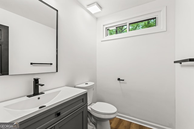 half bathroom featuring toilet, vanity, wood finished floors, and baseboards