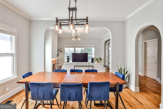 dining space featuring baseboards, ornamental molding, light wood-style floors, arched walkways, and a notable chandelier