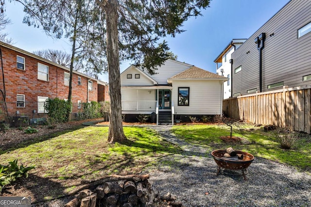 rear view of property featuring a yard, a fire pit, covered porch, and fence