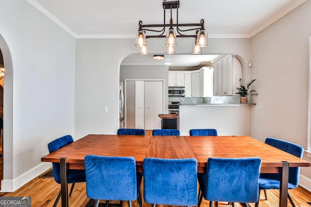 dining room featuring arched walkways, light wood finished floors, and ornamental molding