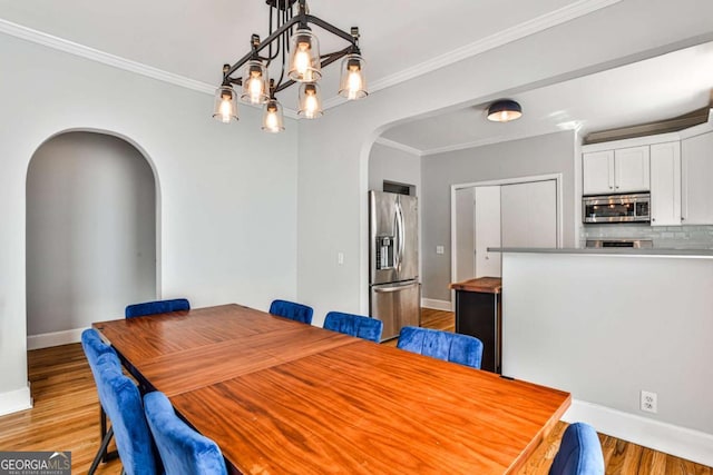 dining room featuring crown molding, light wood-style flooring, baseboards, and arched walkways