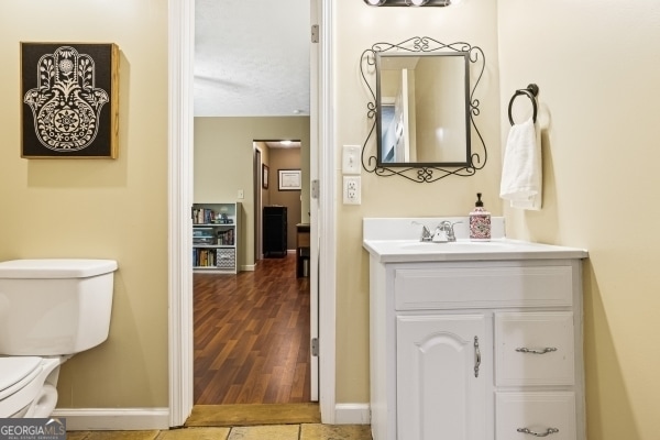 half bathroom featuring vanity, baseboards, toilet, and wood finished floors