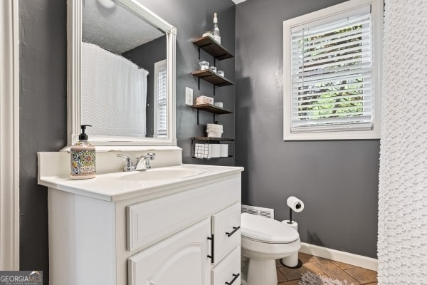 full bathroom with toilet, vanity, and baseboards