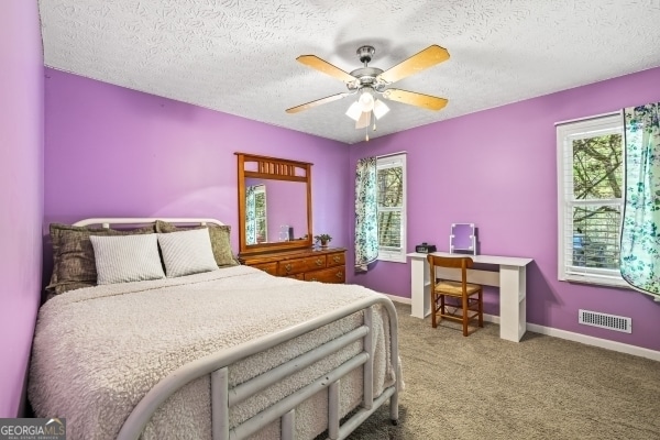 bedroom with ceiling fan, a textured ceiling, visible vents, carpet flooring, and baseboards