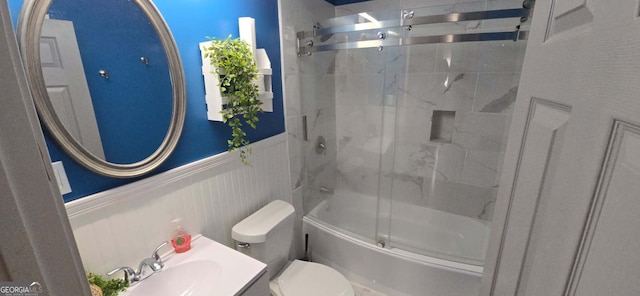 bathroom with a wainscoted wall, combined bath / shower with glass door, toilet, and vanity