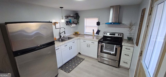 kitchen featuring a sink, decorative backsplash, stainless steel appliances, white cabinets, and wall chimney range hood