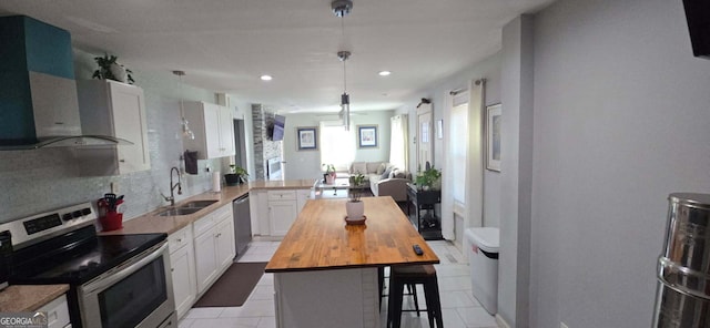 kitchen featuring butcher block countertops, appliances with stainless steel finishes, white cabinetry, wall chimney exhaust hood, and a sink