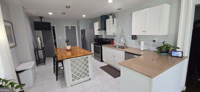 kitchen with wall chimney range hood, butcher block countertops, appliances with stainless steel finishes, white cabinetry, and a sink