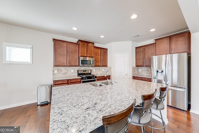 kitchen featuring dark wood-style floors, light stone countertops, a sink, stainless steel appliances, and backsplash