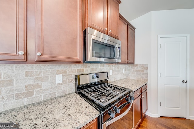 kitchen featuring decorative backsplash, light wood-style flooring, light stone counters, and stainless steel appliances