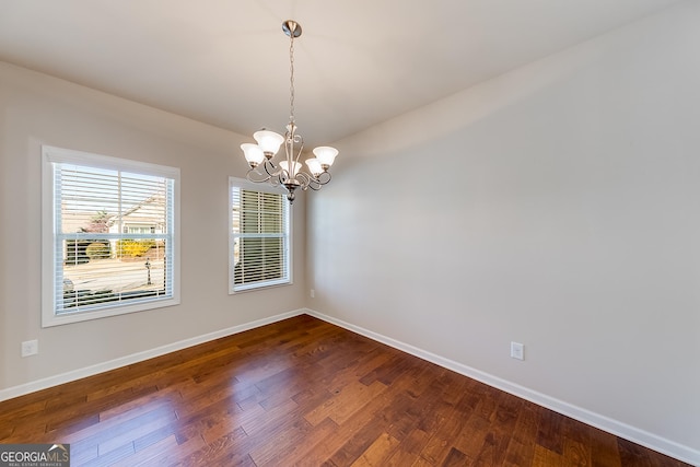 empty room with an inviting chandelier, dark wood-type flooring, and baseboards