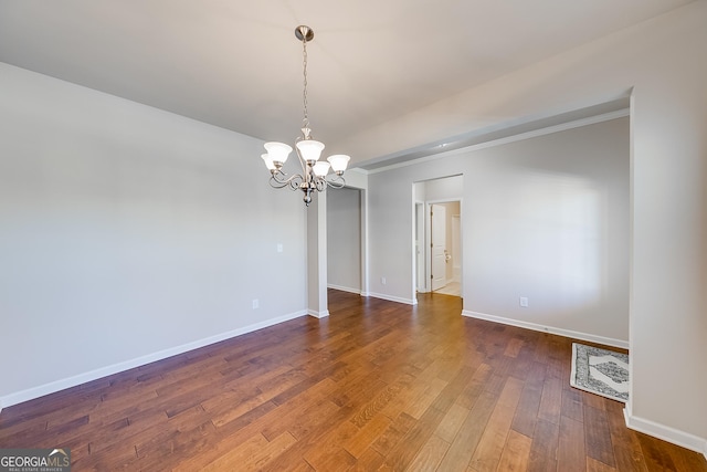 spare room featuring a chandelier, crown molding, baseboards, and hardwood / wood-style flooring