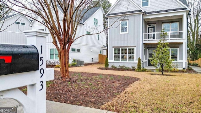 view of front facade with central AC unit, a balcony, board and batten siding, and a front yard