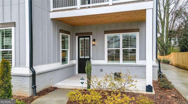 doorway to property featuring brick siding, a balcony, and fence