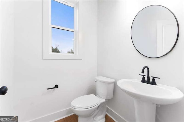 half bath featuring toilet, baseboards, and a sink