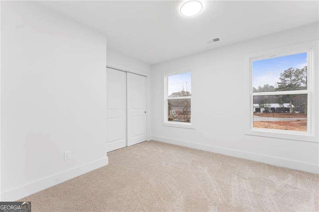 unfurnished bedroom featuring light colored carpet, visible vents, a closet, and baseboards