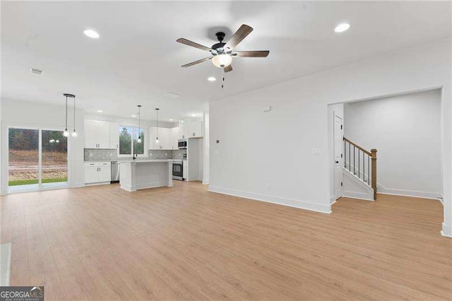 unfurnished living room with stairway, a ceiling fan, baseboards, and light wood finished floors