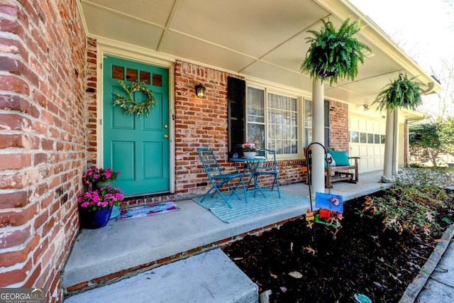 view of exterior entry featuring a porch, an attached garage, and brick siding