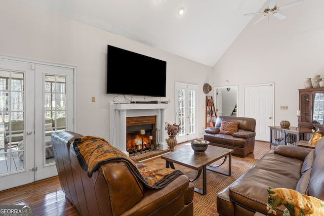 living room featuring high vaulted ceiling, wood finished floors, a brick fireplace, ceiling fan, and stairs