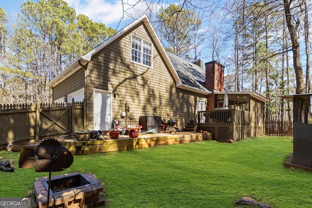 back of house with a chimney, a fenced backyard, a lawn, and an outdoor fire pit