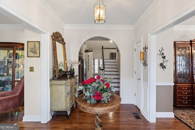 foyer entrance featuring arched walkways, visible vents, ornamental molding, and wood finished floors