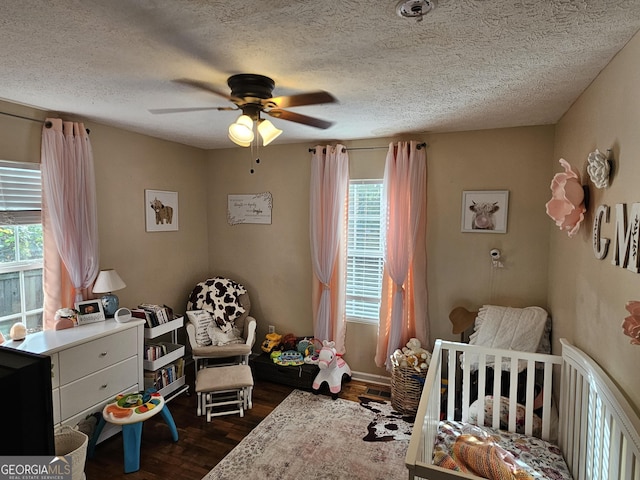 bedroom featuring a textured ceiling, dark wood-type flooring, and a nursery area