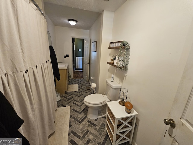 full bathroom with a textured ceiling, toilet, vanity, and brick floor