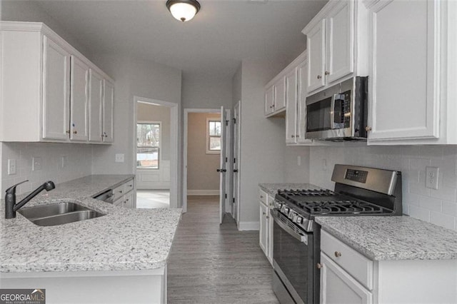 kitchen with a sink, appliances with stainless steel finishes, a peninsula, and white cabinetry