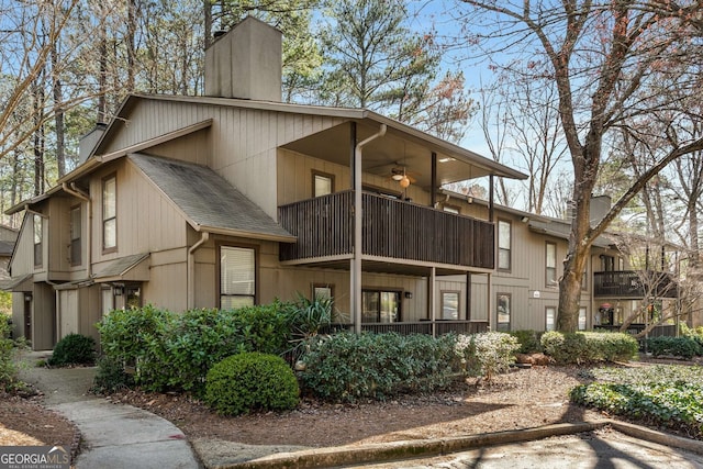 exterior space featuring a chimney, a ceiling fan, a balcony, and roof with shingles