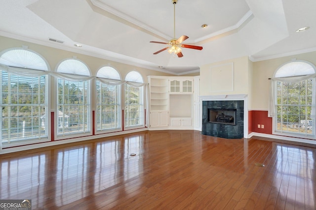 unfurnished living room featuring visible vents, a healthy amount of sunlight, a tray ceiling, a tile fireplace, and wood-type flooring