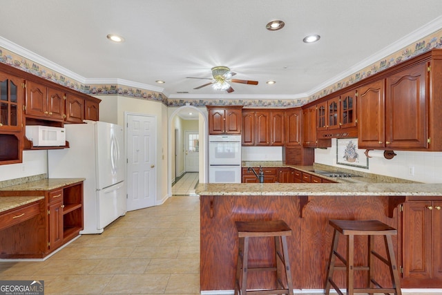 kitchen featuring glass insert cabinets, a peninsula, arched walkways, white appliances, and a ceiling fan