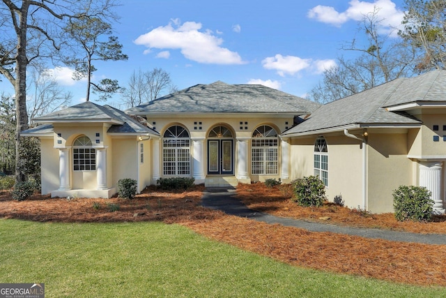 view of front of home with stucco siding, a front lawn, and a shingled roof