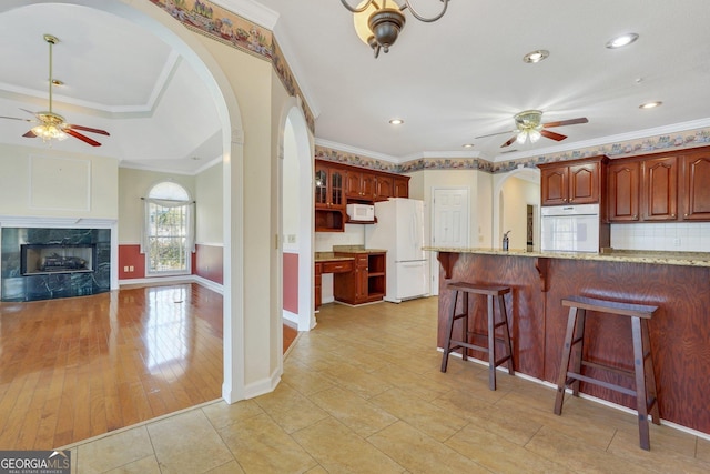 kitchen featuring white appliances, a kitchen breakfast bar, light stone counters, and a ceiling fan