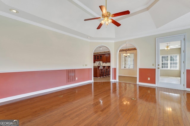 empty room with visible vents, a tray ceiling, hardwood / wood-style floors, ceiling fan with notable chandelier, and arched walkways