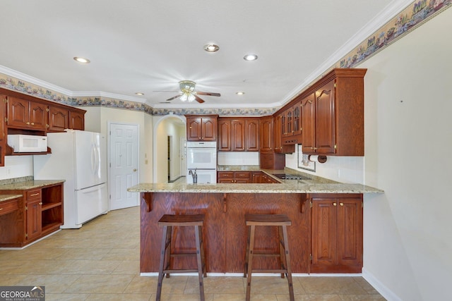 kitchen featuring white appliances, light stone counters, a peninsula, arched walkways, and ceiling fan