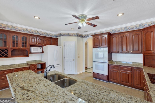 kitchen featuring a sink, white appliances, arched walkways, and light stone countertops