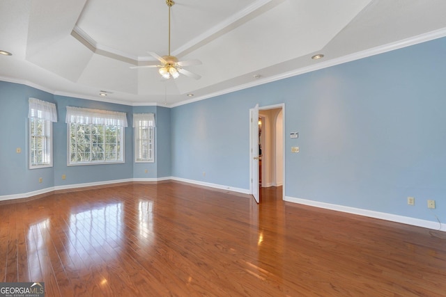 empty room featuring a tray ceiling, wood finished floors, and baseboards