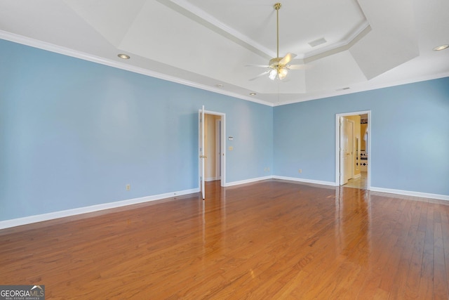 unfurnished room with a raised ceiling, crown molding, wood finished floors, and baseboards