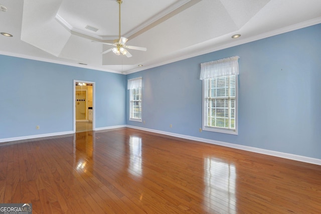 unfurnished room with a raised ceiling, a healthy amount of sunlight, ornamental molding, and hardwood / wood-style flooring